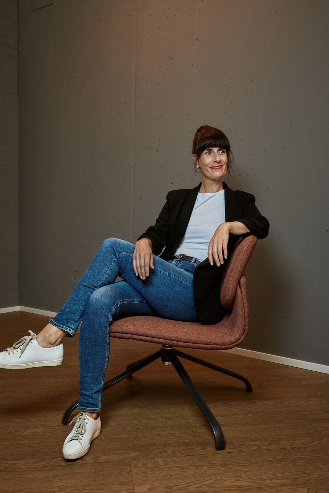 Elvira Häusler sitzt entspannt in einem Sessel vor einer grauen Wand.