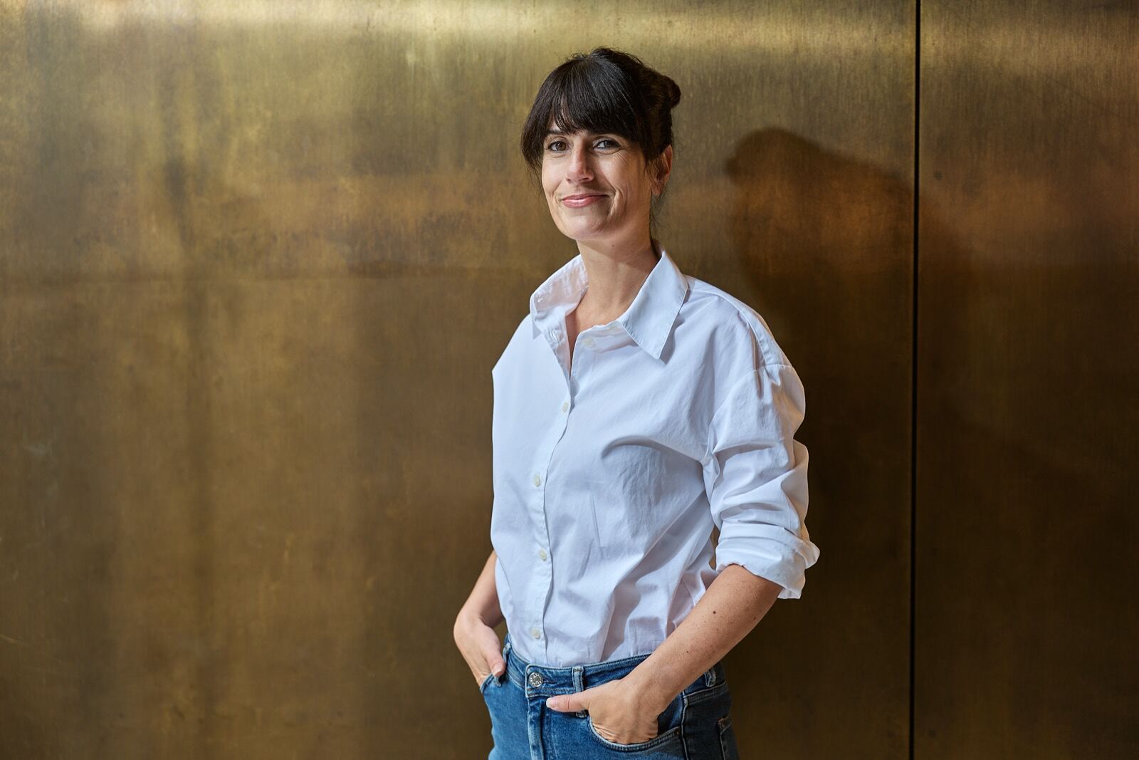 Elvira Häusler in weisser Bluse vor einer Messingwand, ruhiger direkter Blick.
